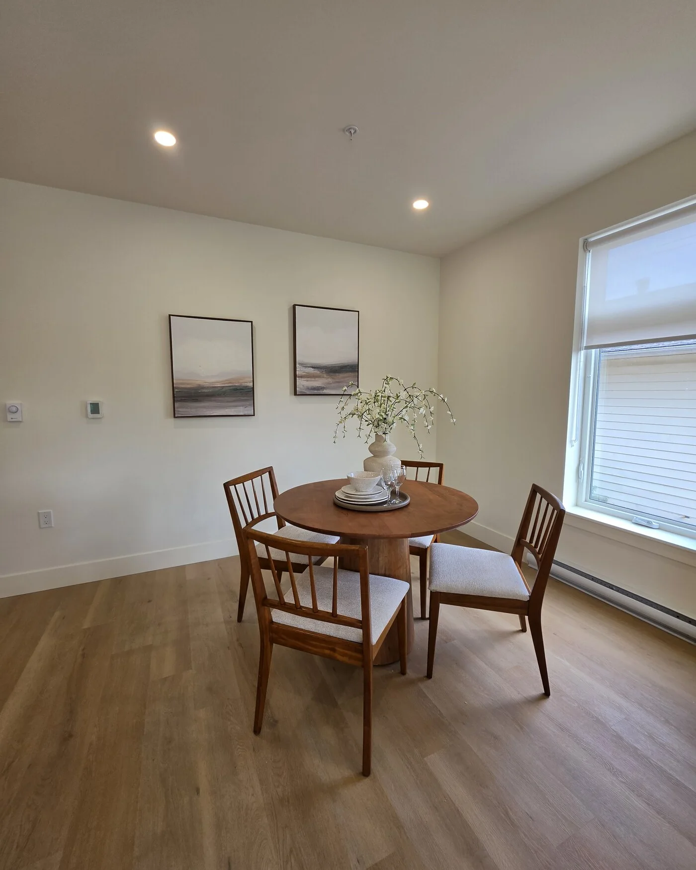 Dining nook with a round wood table, four spindle-back chairs and two framed landscapes